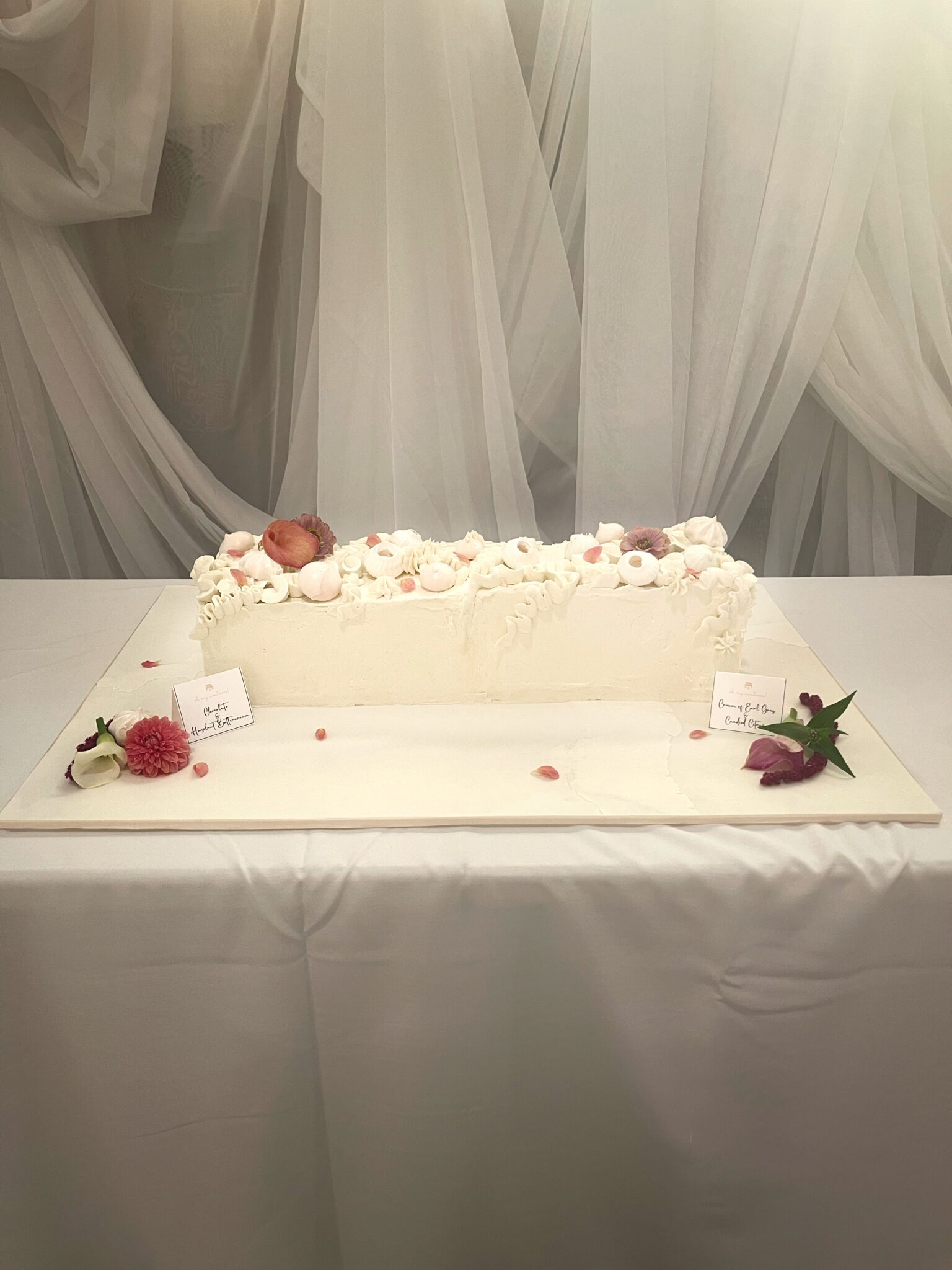 Long rectangular white buttercream celebration cake decorated with delicate flowers and meringue details